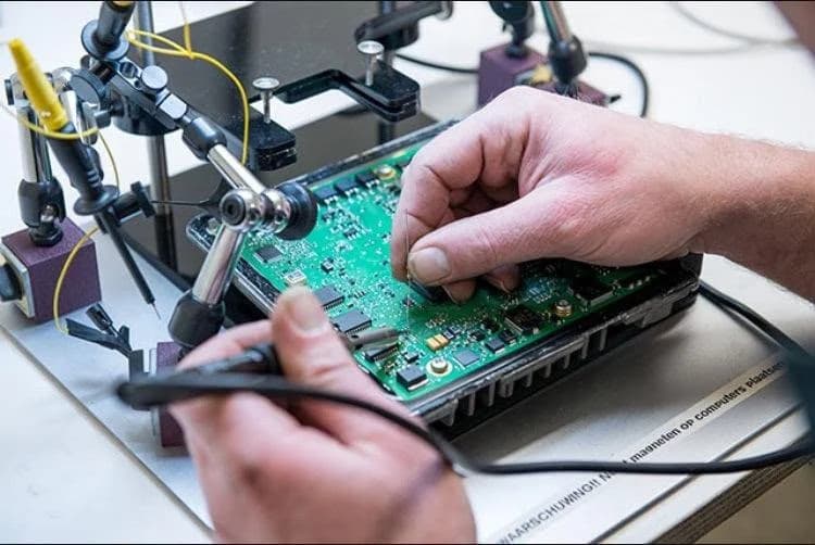 A technician working on an opened control module board held on a bench jig